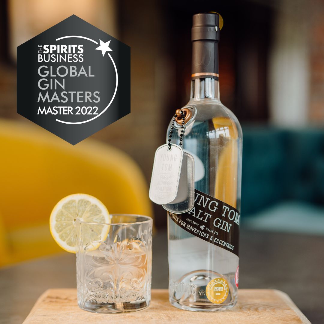 A bottle of gin next to a glass of gin and tonic in an old fashioned glass garnished with a slice of lemon
